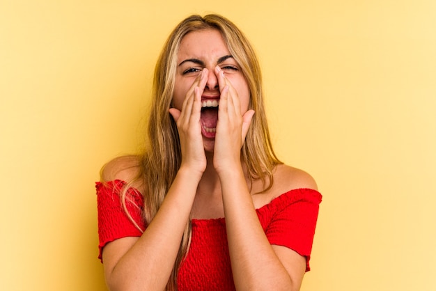 Jovem mulher loira caucasiana isolada em fundo amarelo gritando animado para a frente.