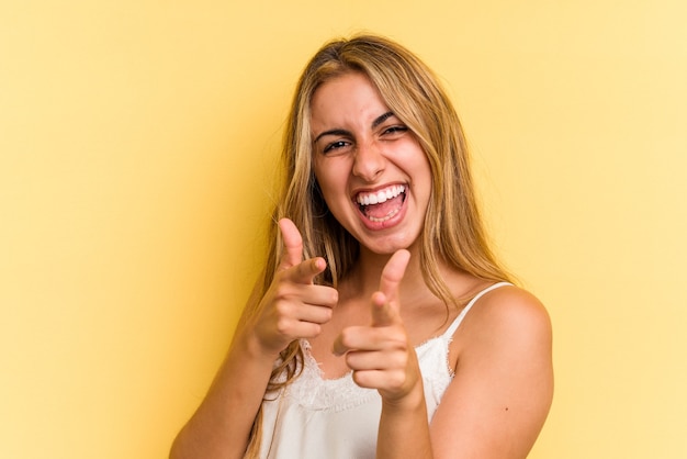 Jovem mulher loira caucasiana isolada em um fundo amarelo, apontando para a frente com os dedos.