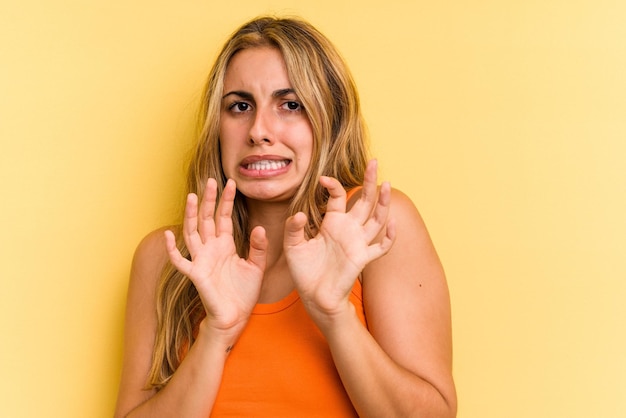 Jovem mulher loira caucasiana, isolada em um fundo amarelo, rejeitando alguém mostrando um gesto de nojo.