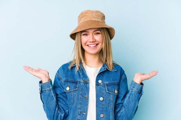 Jovem mulher loira caucasiana isolada faz escala com os braços, sente-se feliz e confiante.