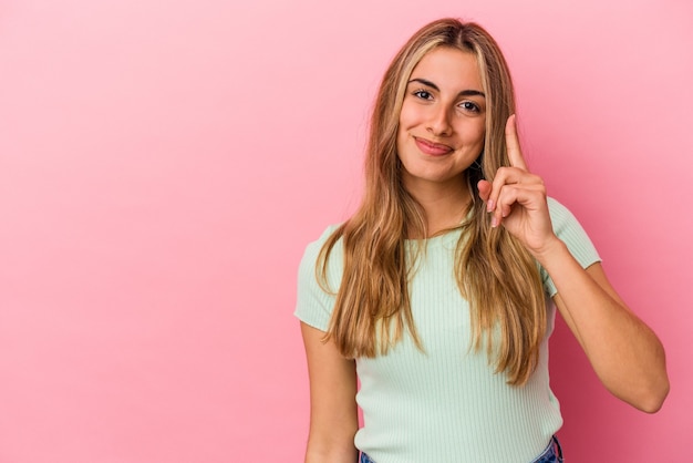 Jovem mulher loira caucasiana isolada na parede rosa mostrando o número um com o dedo