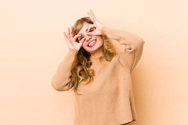 Jovem mulher loira caucasiana mostrando sinal positivo sobre os olhos