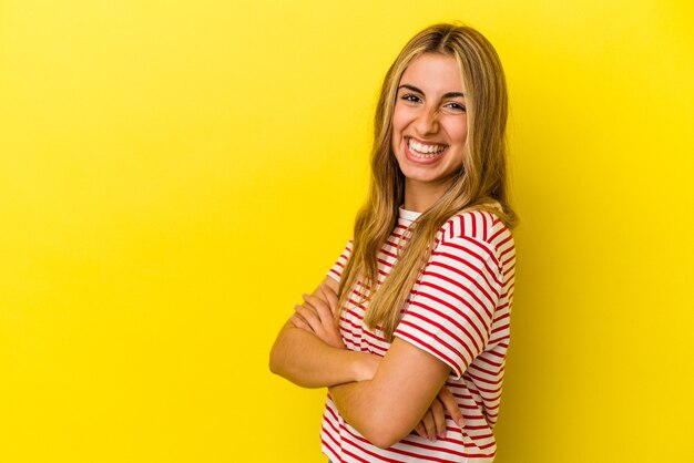 Jovem mulher loira caucasiana, sorrindo confiante com os braços cruzados.