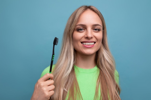 Jovem mulher loira com dentes saudáveis, segurando uma escova de dentes em um fundo azul