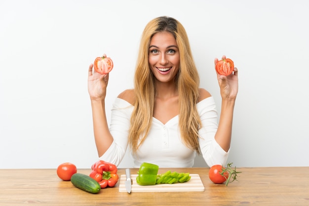 Jovem mulher loira com legumes em uma mesa