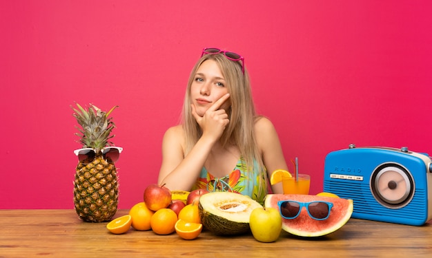 Jovem mulher loira com muitas frutas, pensando em uma idéia