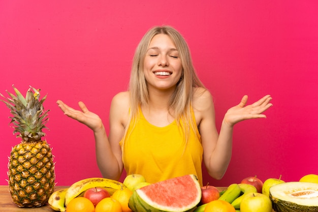 Jovem mulher loira com muitas frutas rindo