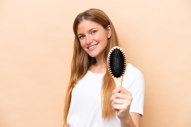 Jovem mulher loira com pente de cabelo isolado em fundo bege com expressão feliz