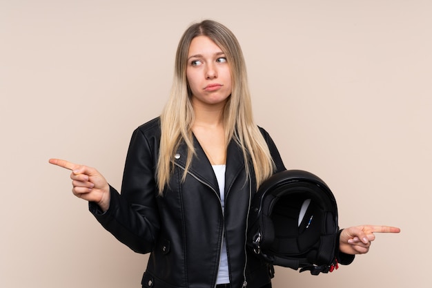 Jovem mulher loira com um capacete de moto, apontando para as laterais, tendo dúvidas