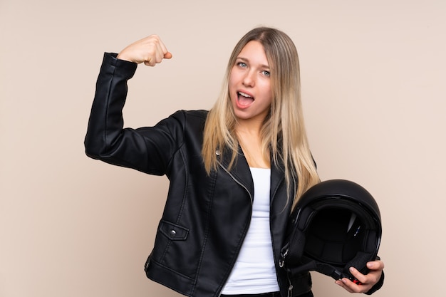 Foto jovem mulher loira com um capacete de moto sobre parede isolada, fazendo um gesto forte