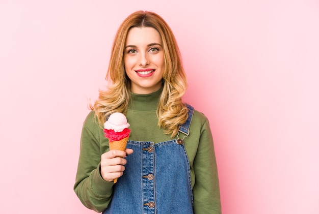 Jovem mulher loira comendo um sorvete isolado feliz, sorridente e alegre.