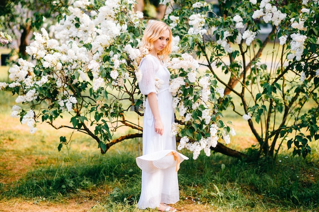 Jovem mulher loira de vestido branco, posando no parque ensolarado.