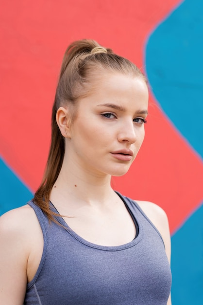 Jovem mulher loira em roupas esportivas em retrato de treinamento ao ar livre, plano de fundo multicolorido