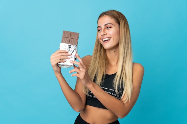 Jovem mulher loira em um fundo isolado tomando uma pastilha de chocolate e feliz