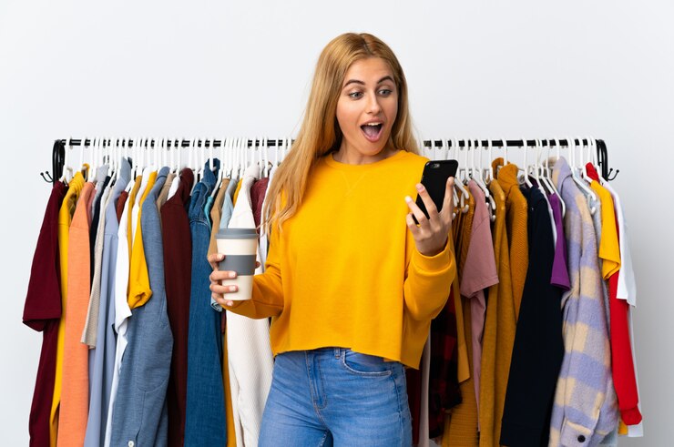 Foto jovem mulher loira em uma loja de roupas segurando café para levar e um celular
