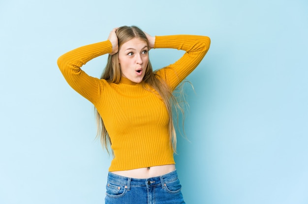 Jovem mulher loira isolada na parede azul gritando, muito animada, apaixonada, satisfeita com alguma coisa.