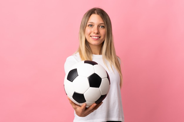 Jovem mulher loira isolada na parede rosa com bola de futebol