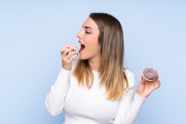 Jovem mulher loira isolado parede azul comendo um donut