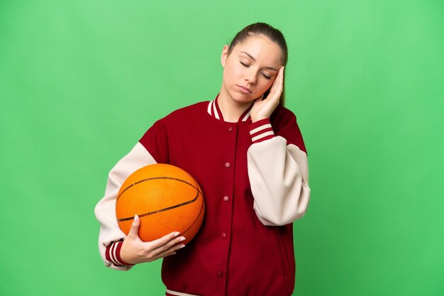 Jovem mulher loira jogando basquete sobre fundo croma isolado com dor de cabeça