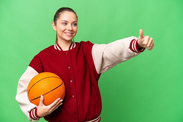 Jovem mulher loira jogando basquete sobre fundo croma isolado dando um polegar para cima gesto