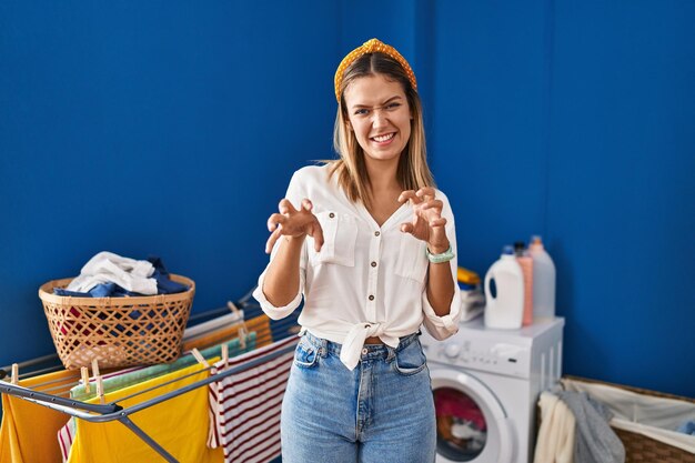 Foto jovem mulher loira na lavandaria sorrindo engraçado fazendo gesto de garra como gato expressão agressiva e sexy