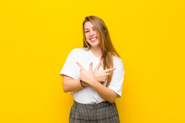 Jovem mulher loira olhando confusa e confusa, insegura e apontando em direções opostas, com dúvidas sobre a parede laranja