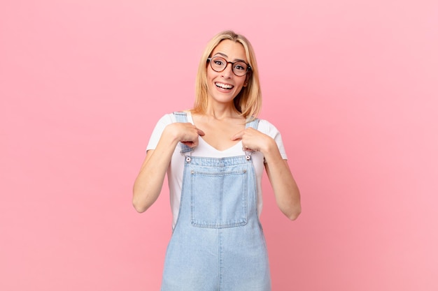 Jovem mulher loira se sentindo feliz e apontando para si mesma com um animado