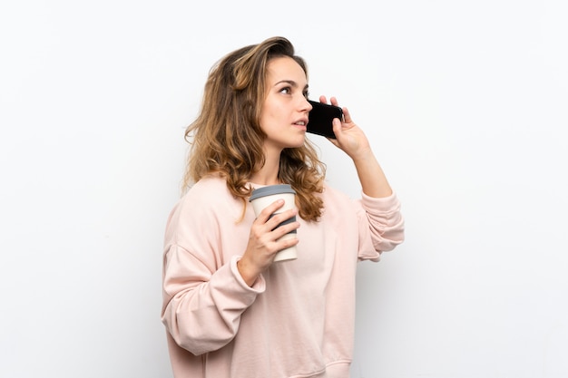 Jovem mulher loira segurando café para levar e um celular