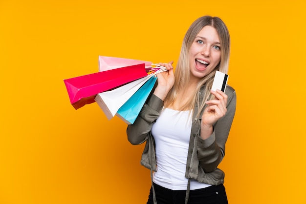 Jovem mulher loira segurando sacolas de compras e um cartão de crédito