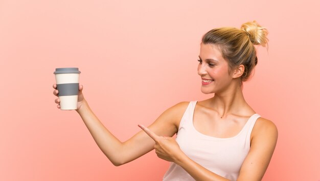 Jovem mulher loira segurando um café e apontando-o