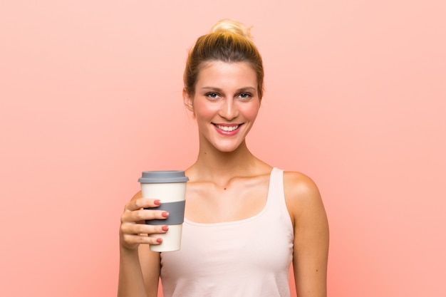 Jovem mulher loira segurando um café para viagem sorrindo muito