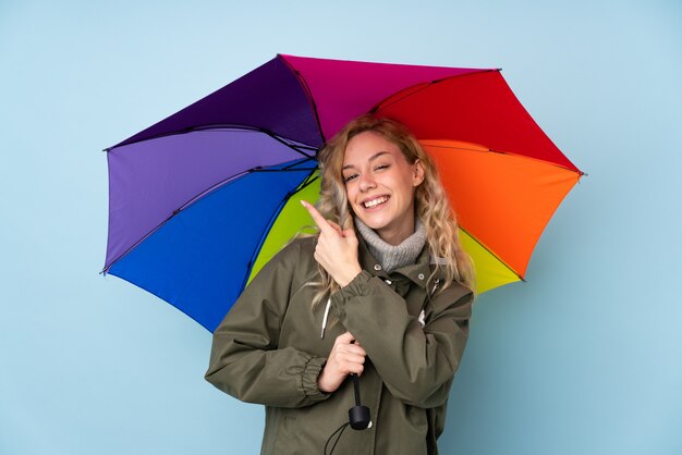 Jovem mulher loira segurando um guarda-chuva em azul e apontando-o