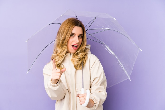 Jovem mulher loira segurando um guarda-chuva isolado Jovem mulher loira segurando um guarda-chuva isolado, tendo uma ideia, o conceito de inspiração.