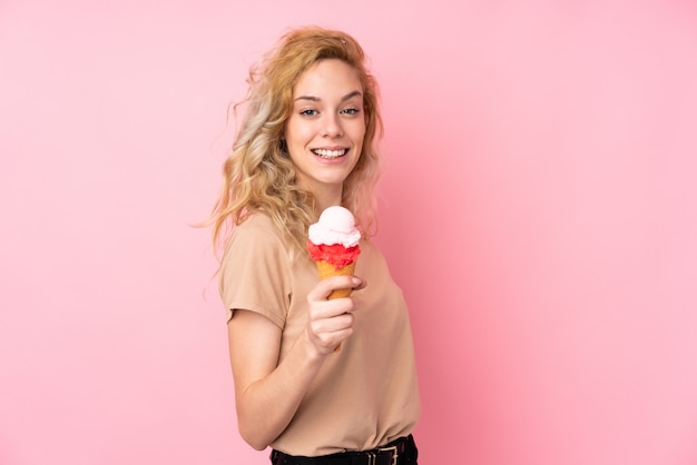 Jovem mulher loira segurando um sorvete de corneta isolado na parede rosa com expressão feliz