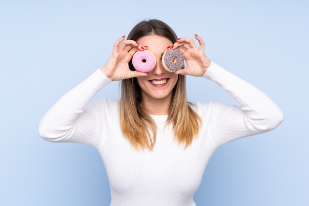 Jovem mulher loira sobre parede isolada segurando rosquinhas nos olhos