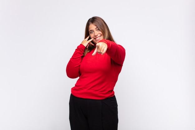 Jovem mulher loira sorrindo alegremente e apontando enquanto faz um gesto depois de ligar para você, falando ao telefone