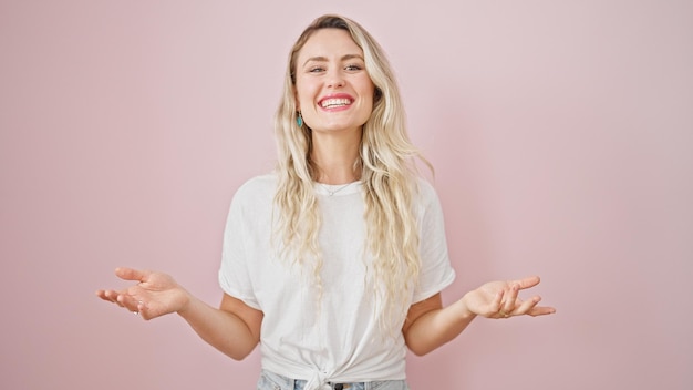 Jovem mulher loira sorrindo confiante falando sobre fundo rosa isolado