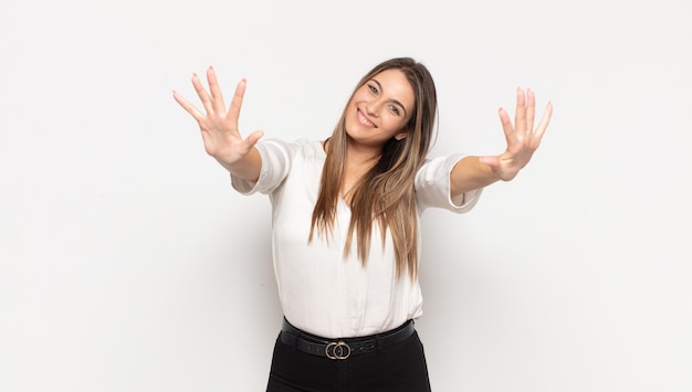 Jovem mulher loira sorrindo e parecendo amigável, mostrando o número dez ou décimo com a mão para a frente, em contagem regressiva