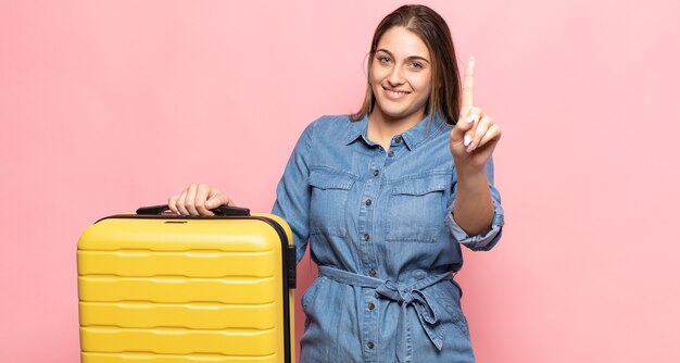 Jovem mulher loira sorrindo e parecendo amigável, mostrando o número um ou primeiro com a mão para a frente, em contagem regressiva