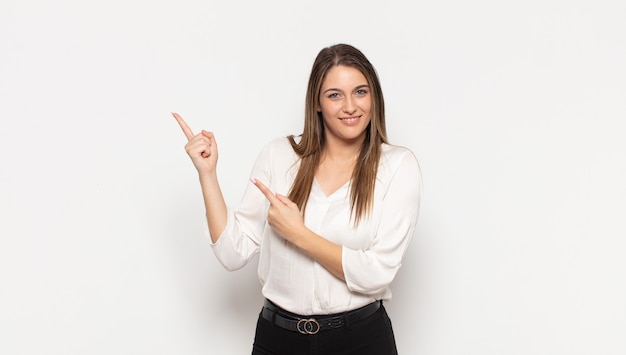 Jovem mulher loira sorrindo feliz e apontando para o lado e para cima com as duas mãos mostrando o objeto no espaço da cópia