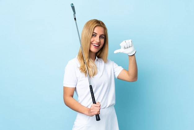 Jovem mulher loira uruguaia sobre parede azul isolada jogando golfe e orgulhosa de si mesmo