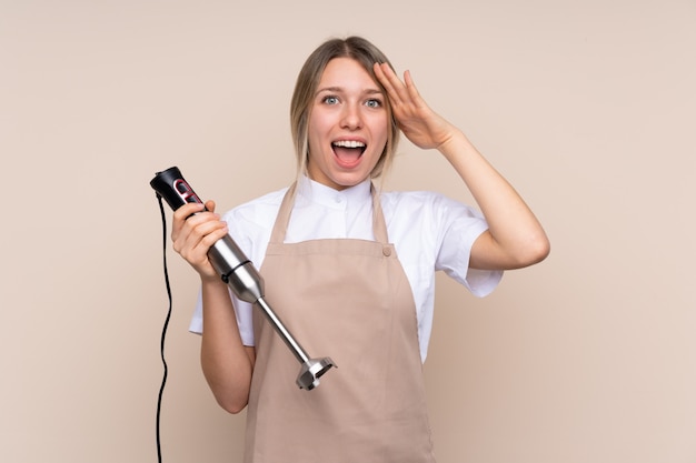 Jovem mulher loira usando o liquidificador com surpresa e expressão facial chocada