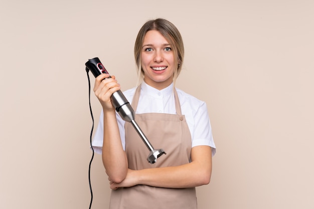 Jovem mulher loira usando o liquidificador, sorrindo muito