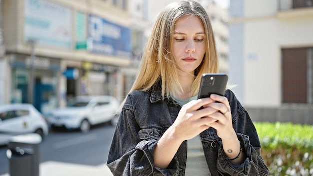 Jovem mulher loira usando smartphone com cara séria na rua