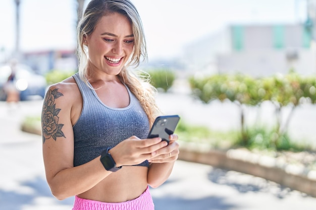 Jovem mulher loira vestindo roupas esportivas usando smartphone na rua