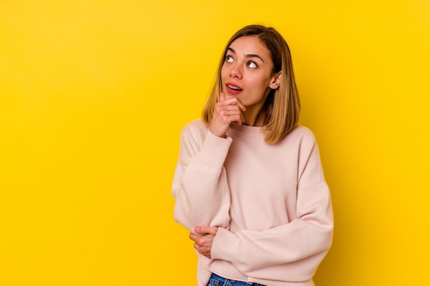 Jovem mulher magra caucasiana isolada no amarelo relaxado pensando em algo olhando para um espaço de cópia.