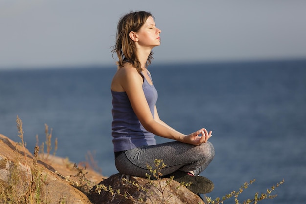 Jovem mulher meditando sobre a rocha perto da beira-mar. Exercício de ioga na costa do mar.