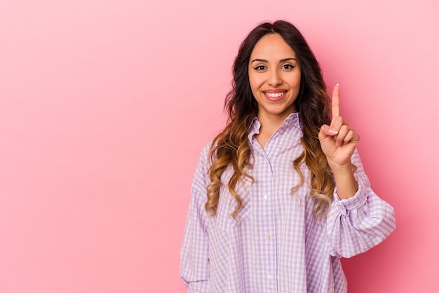 Jovem mulher mexicana isolada em um fundo rosa, mostrando o número um com o dedo.