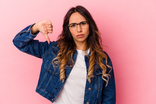 Jovem mulher mexicana isolada em um fundo rosa, mostrando o polegar para baixo, o conceito de decepção.