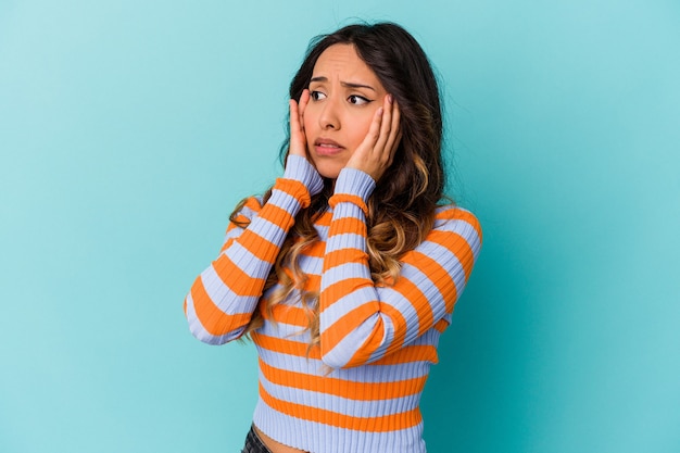 Jovem mulher mexicana isolada na parede azul com medo e medo.